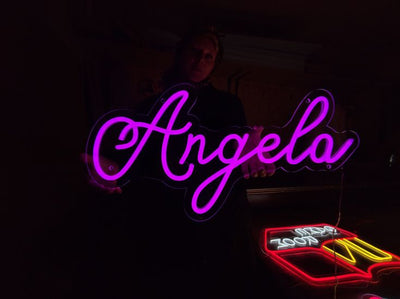 Angela Name Neon sign by Neon.Outshine  - in glowing cursive, mounted on clear acrylic and illuminating a chic, modern space with vibrant light.
