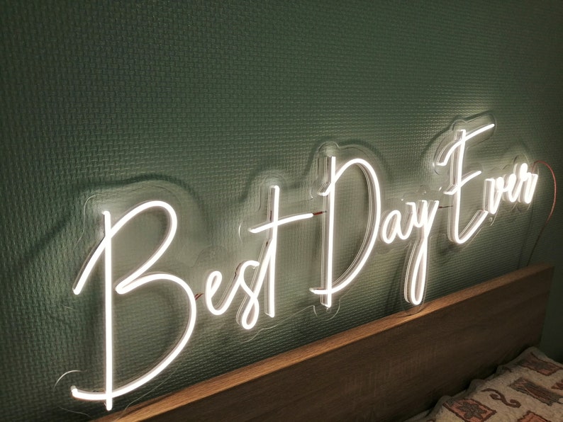 Best Day Ever LED neon sign glowing in white against a floral wedding backdrop   designed by Neon.Outshine for celebrations and events.