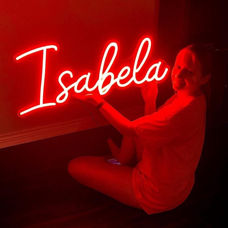 Isabella Name Neon sign By Neon.Outshine - in elegant script, casting a soft pink light on a bedroom wall.