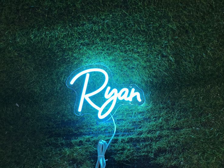 Ryan Name Neon sign in stylish script, mounted on a clear acrylic panel and radiating vibrant light against a modern interior wall - Neon.Outshine 