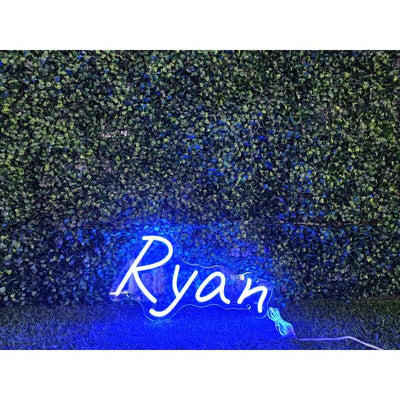 Ryan Name Neon sign in stylish script, mounted on a clear acrylic panel and radiating vibrant light against a modern interior wall - Neon.Outshine 