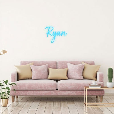 Ryan Name Neon sign in stylish script, mounted on a clear acrylic panel and radiating vibrant light against a modern interior wall - Neon.Outshine 