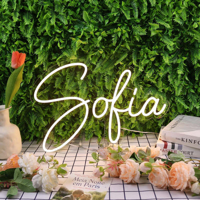Sofia Name Neon sign by Neon.Outshine - in glowing cursive letters, mounted on clear acrylic and softly lighting a feminine, modern interior.