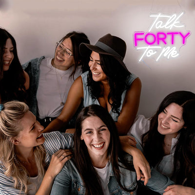 Talk Forty To Me LED neon sign in hot pink, glowing on a party wall  - designed by Neon.Outshine for 40th birthday celebrations.