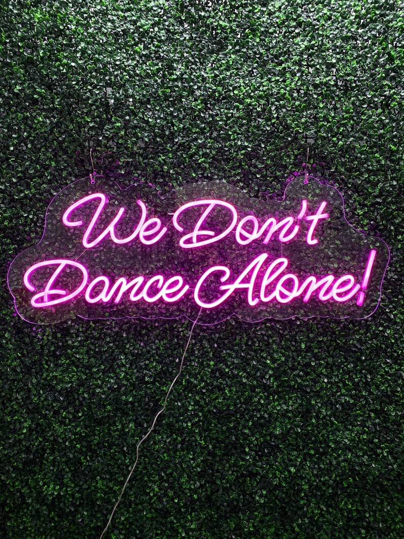 We Don’t Dance Alone neon sign in vivid LED glow, mounted on acrylic, lighting up a party or dance space – by Neon.Outshine.