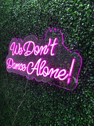 We Don’t Dance Alone neon sign in vivid LED glow, mounted on acrylic, lighting up a party or dance space – by Neon.Outshine.