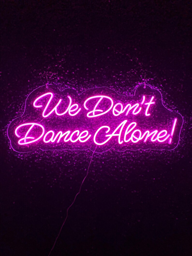 We Don’t Dance Alone neon sign in vivid LED glow, mounted on acrylic, lighting up a party or dance space – by Neon.Outshine.