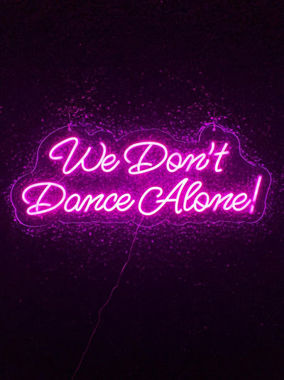 We Don’t Dance Alone neon sign in vivid LED glow, mounted on acrylic, lighting up a party or dance space – by Neon.Outshine.